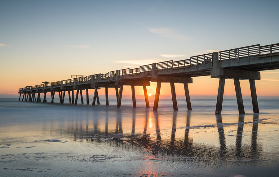 sunrise seen through pier on smooth surf beach in jacksonville