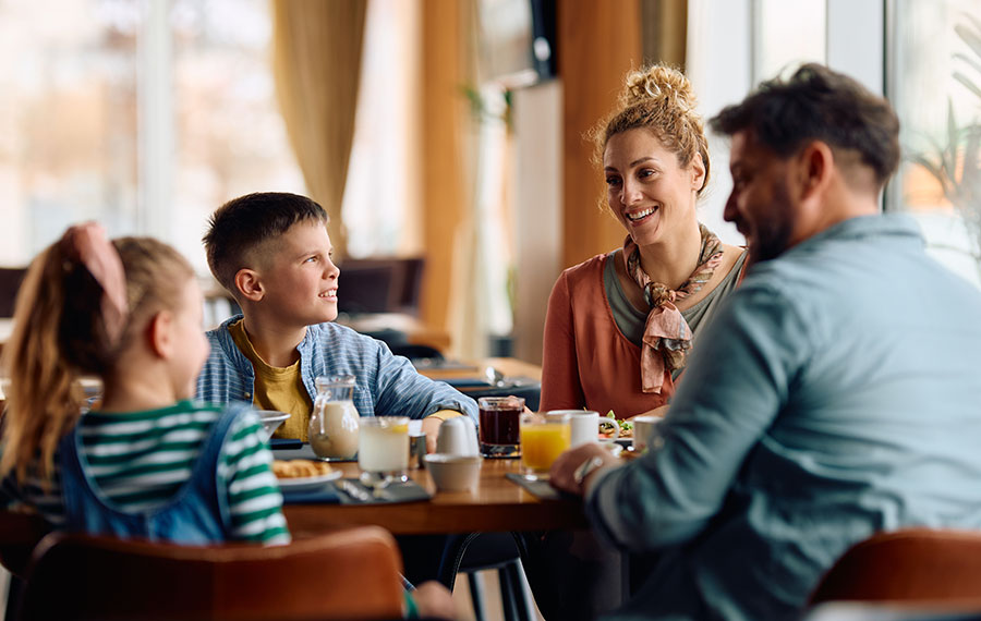 family of four talking at restaurant table while having breakfast